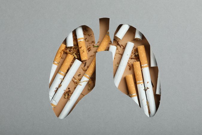 Lung shape cut out of grey paper with cigarettes