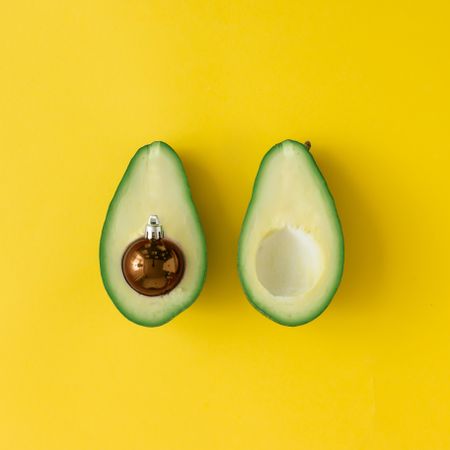 Avocado with brown bauble decoration in place of pit on bright yellow background