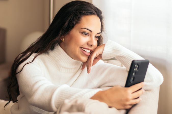 Connected at Home: Young Woman Sitting on Sofa Using Smartphone