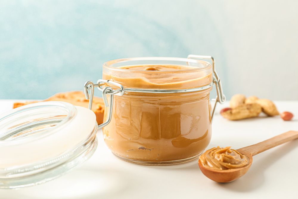 Composition with peanut butter sandwich, glass jar, peanut and spoon on light table against light background, space for text and closeup
