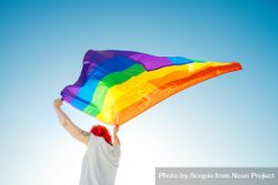 Young woman in light top waving rainbow flag under blue sky 0yQea0