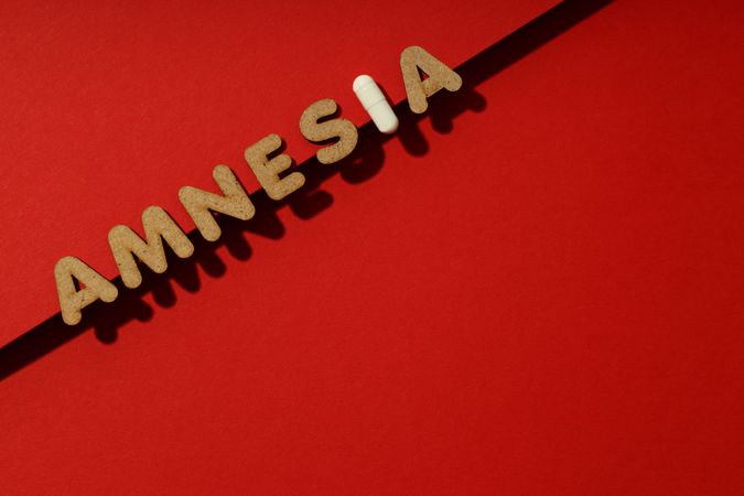 Cork letters of the word “Amnesia” with pill on red background with copy space