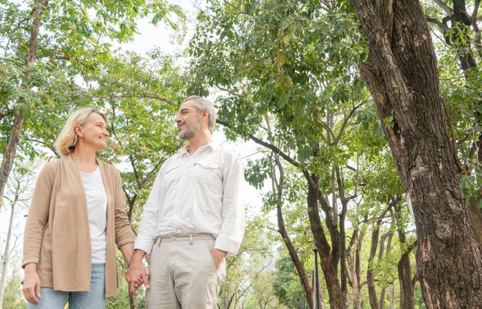 Mature man and woman walking hand in hand in park