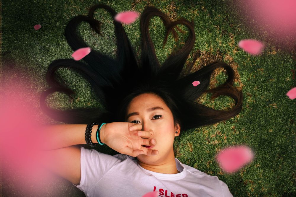 Girl with hair shaped into hearts lying on green grass with flower petal floating