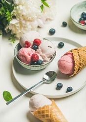 Scoops of ice cream in bowl and in waffle cones with berries