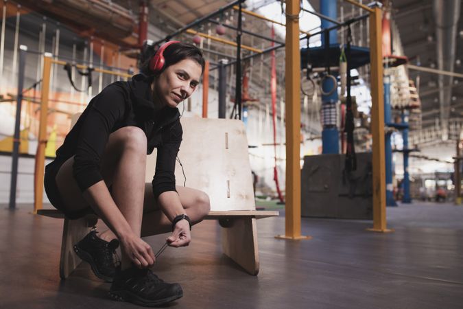 Smiling woman with headphones lacing shoe in gym