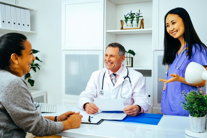 Happy doctor and nurse discussing medical file with patient in office