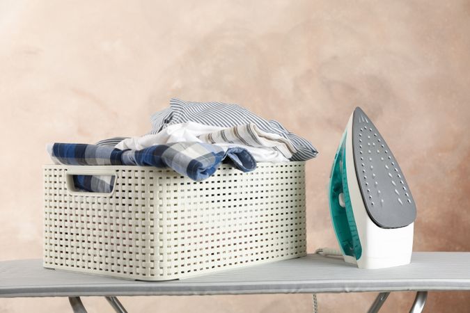 Basket with clean laundry and iron on ironing board, space for text