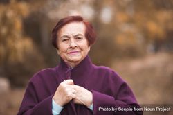 Portrait of older woman in purple coat standing near yellow trees 4mK8X0