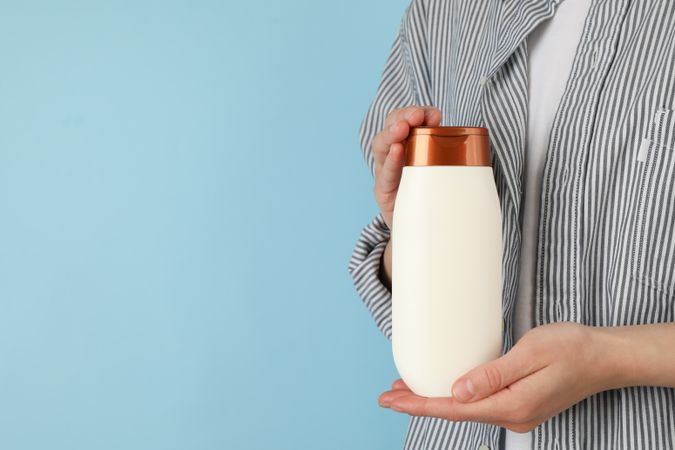 Woman holds blank shampoo bottle on blue background, space for text