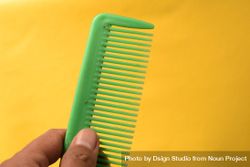 Hand holding bright green hair comb against yellow background 4329eV