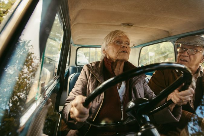 Woman with gray hair driving a car and talking with her husband sitting in passenger seat