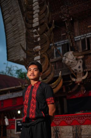 Young man from Tara Toraja community standing beside their traditional wooden house