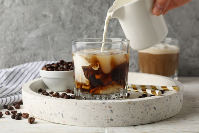 Woman pours a milk in glass of coffee. Composition with ice coffee