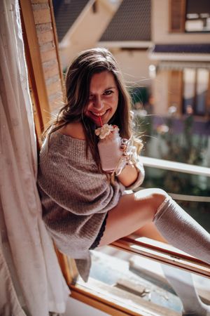 Young woman sitting with tasty drink on window