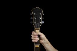 Hand gripping the neck of an electric guitar on a dark background.