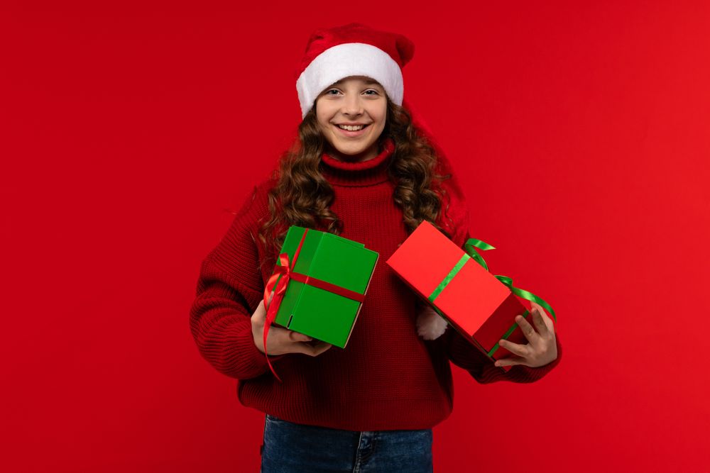 Smiling girl in Santa hat holds two gift boxes.