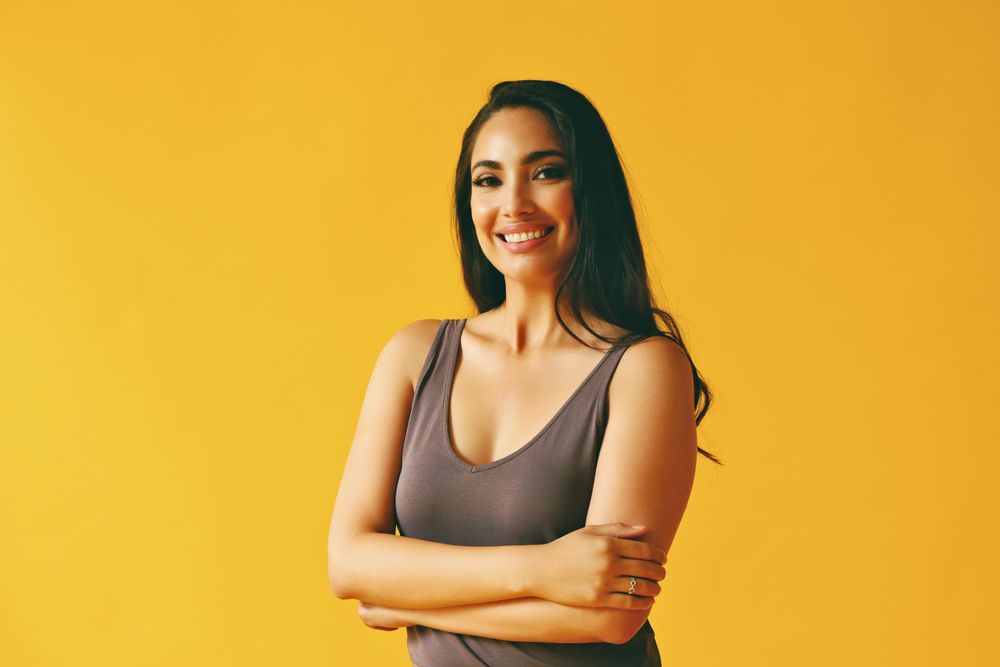 Confident smiling Hispanic woman standing and looking at camera in yellow room, copy space