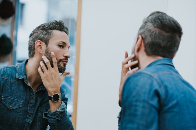 Man looking at mirror and touching beard in salon