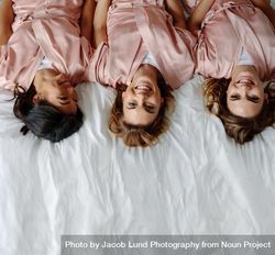Top view of bride with female friends lying on bed and smiling 4AeW84