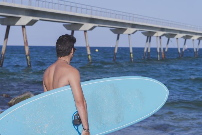 Male surfer standing in the rocks on the coast near pier