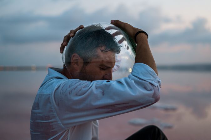 Man with fish tank on head sitting at seashore
