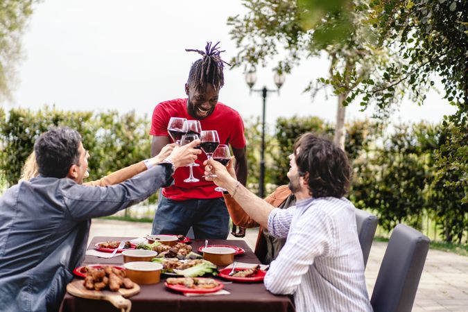 Diverse group of friends laughing and toasting with red wine at an outdoor table filled with delicious food