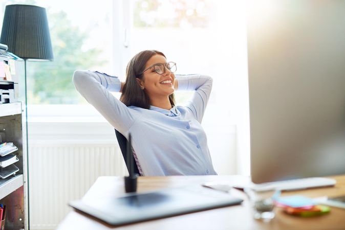 Smiling female sitting at her desk with her hands behind her head