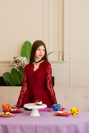 Teenage girl in red lace dress standing by table