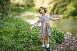 Child in dress looking away from the river with her arms open