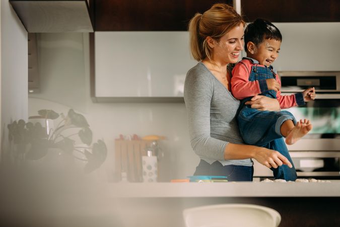 Smiling woman holding his son in her arms while making cookies in kitchen