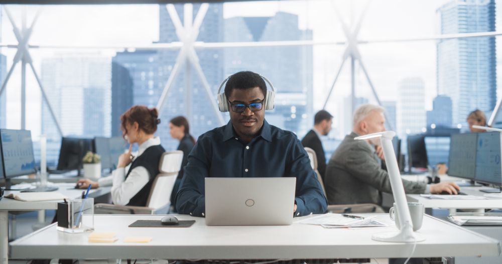 Successful Black Man Wearing Headphones And Starts Typing On Laptop