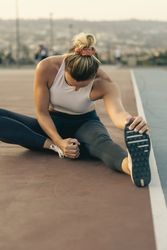Sporty woman from behind stretching her hamstring on a running track