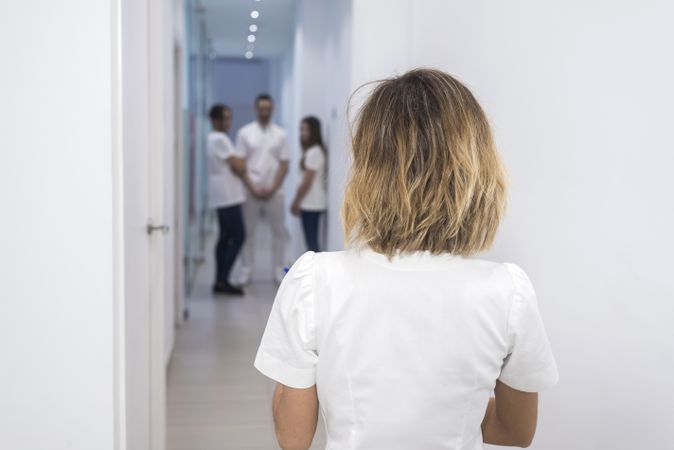 Back of female doctor in uniform, walking in the corridor of hospital with medical team blurred far away
