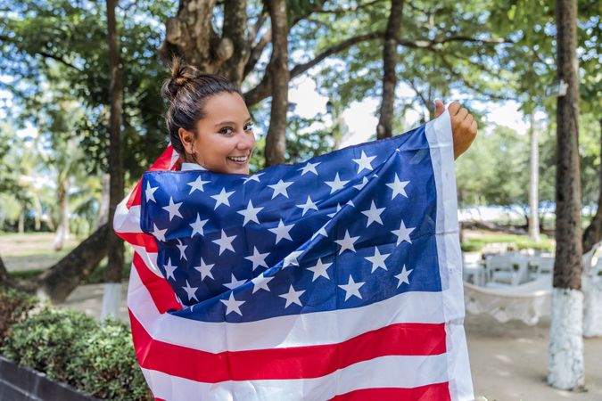 Content woman smiling wrapped in American flag walking along park
