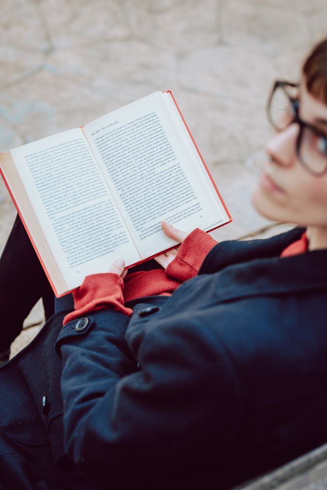 Young woman reading book on bench in park