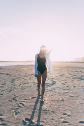 Female standing on beach with sunset at her back with bright sun