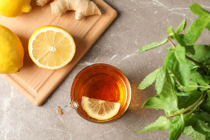 Cup of tea, lemon, ginger and mint on grey background, top view