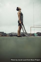 Muscular man doing fitness workout outdoors in rain with battle ropes on field 5rq1d0