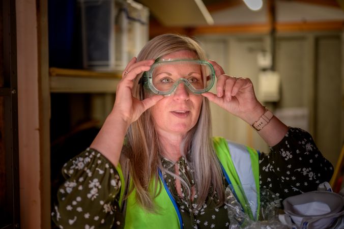 Mature woman putting on safety glasses in stock room