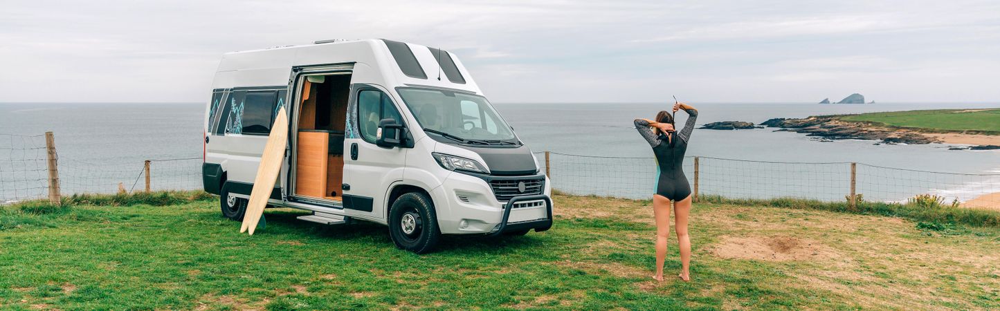 Female zipping up her wetsuit outside of motorhome parked on the coast