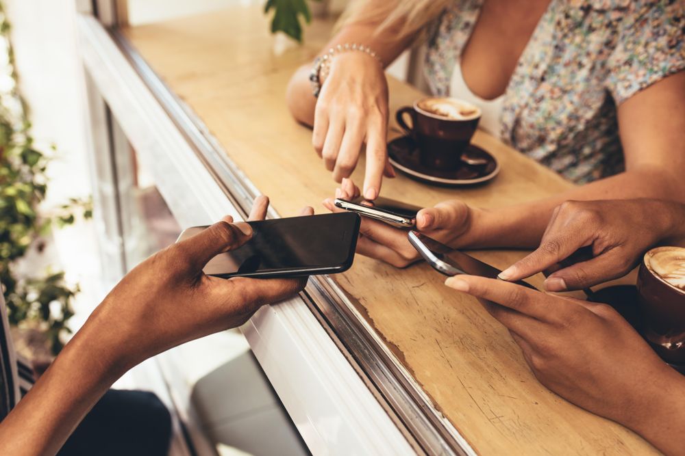 Cropped shot of young people connecting their devices at coffee shop