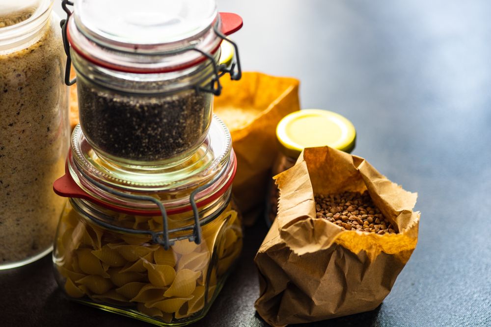 Containers of dried legumes and pasta from pantry with copy space