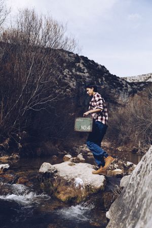 Woman with case jumping on rocks above stream