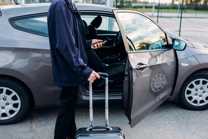 Man about to enter car with suitcase and smartphone in hand