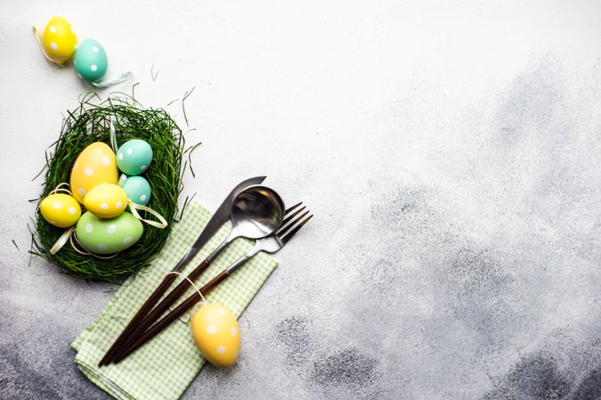 Easter festive card concept with pastel egg decorations on grey table with silverware