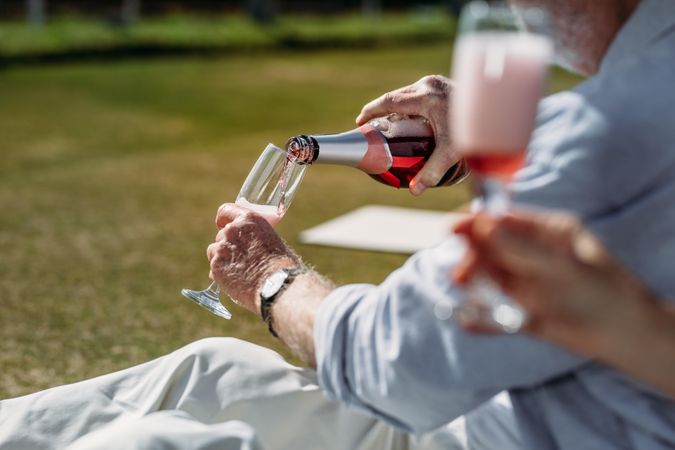 Close up of a man pouring drinks in a glass sitting outdoors in a park