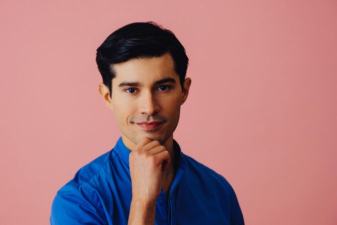 Contemplative Latino man in pink studio with hand on chin