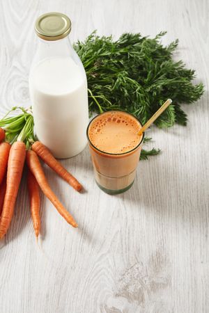 Top view of carrot juice with bunch of carrots and bottle of milk