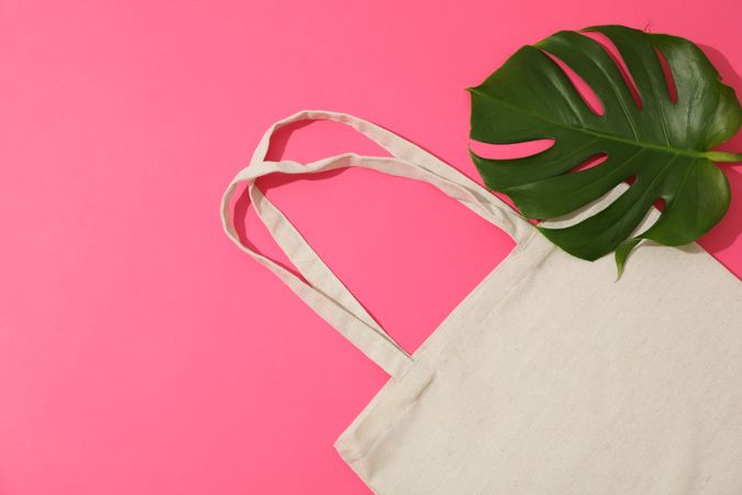 Eco bag and palm leaves on color background, top view